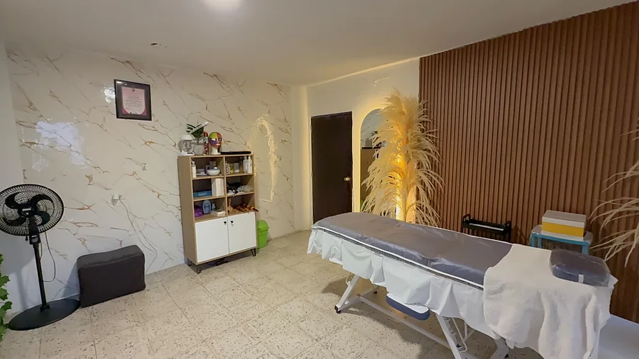 Cabina de Belleza Sobrenatural: pared de mármol, mueble de productos, camilla y lámpara de pampas