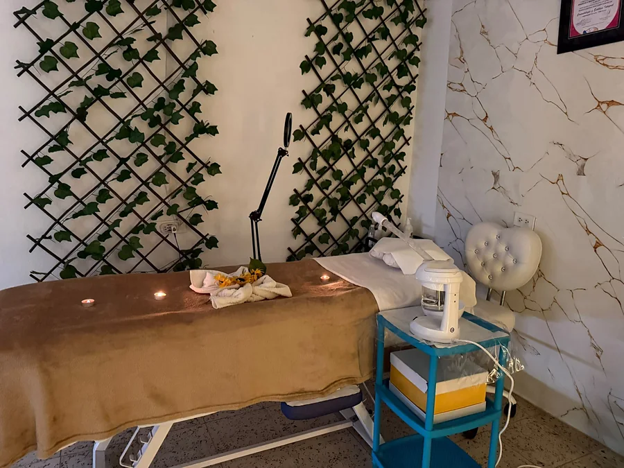 Camilla preparada con velas, toalla con girasoles y vaporizador facial junto a la pared de enredaderas