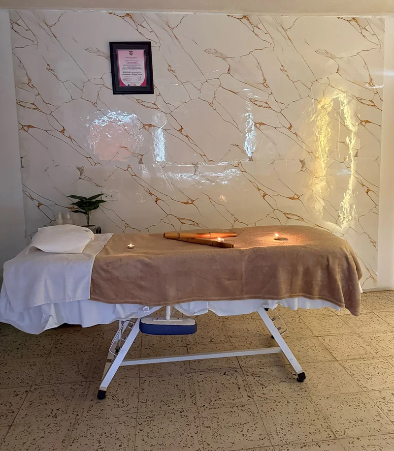 Camilla con manta, velas encendidas y cañas de bambú frente a la pared de mármol de la cabina de Belleza Sobrenatural